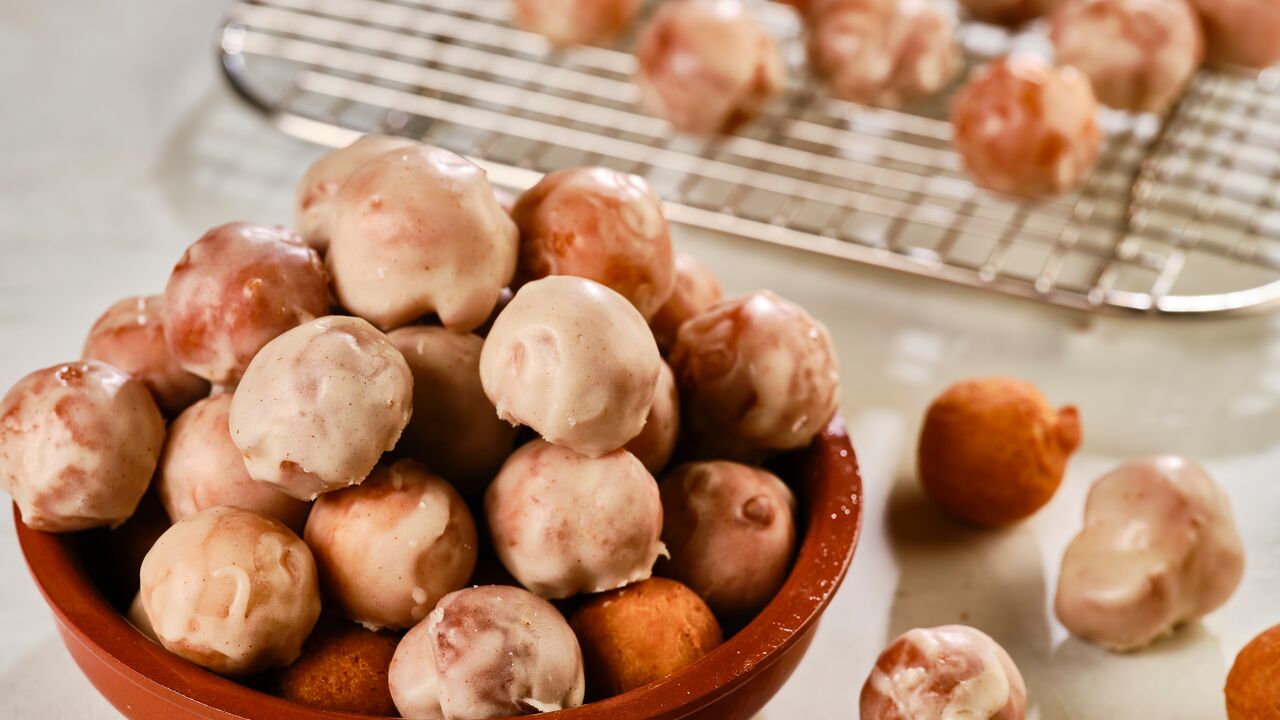 frosted donut holes in a bowl, on a cooling rack, and scattered on a counter