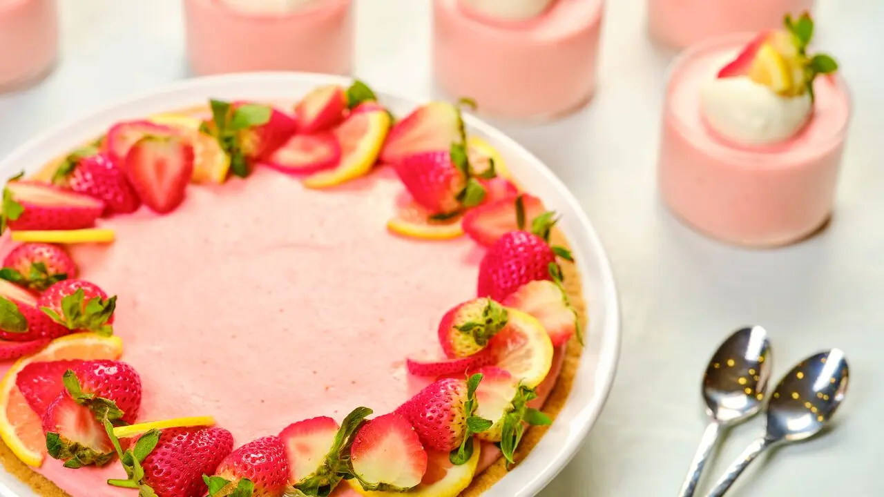 A strawberry lemon pie displayed on a countertop surrounded by smaller cups of pie filling and two spoons